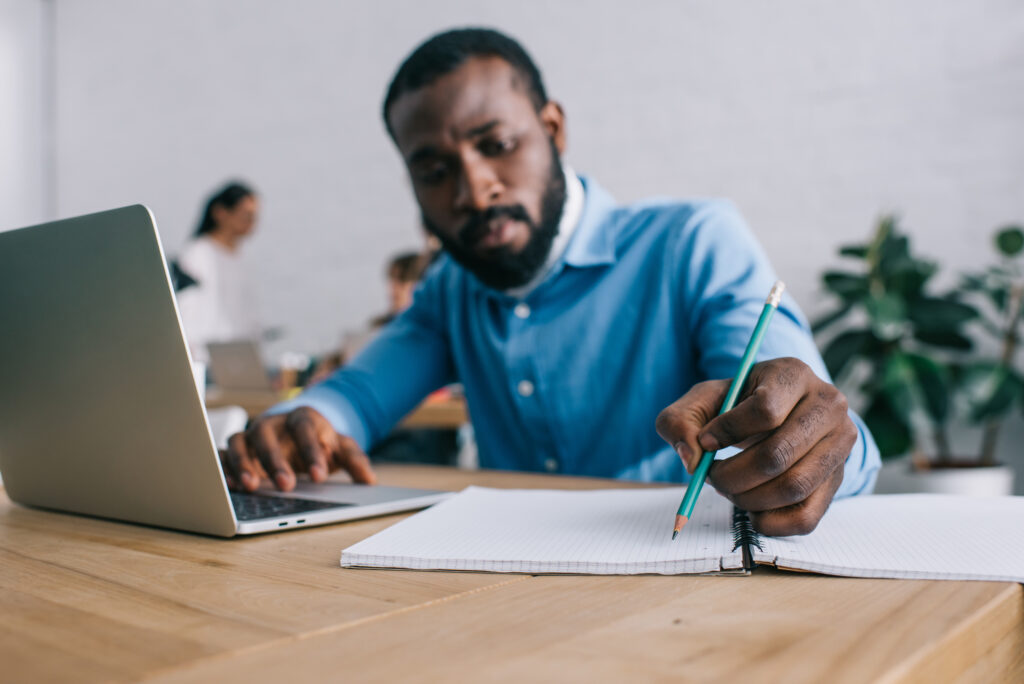 Man writing a job description using laptop and paper.